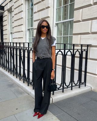 @symphonyofsilk wearing black tailored trousers, sweater vest and red heels