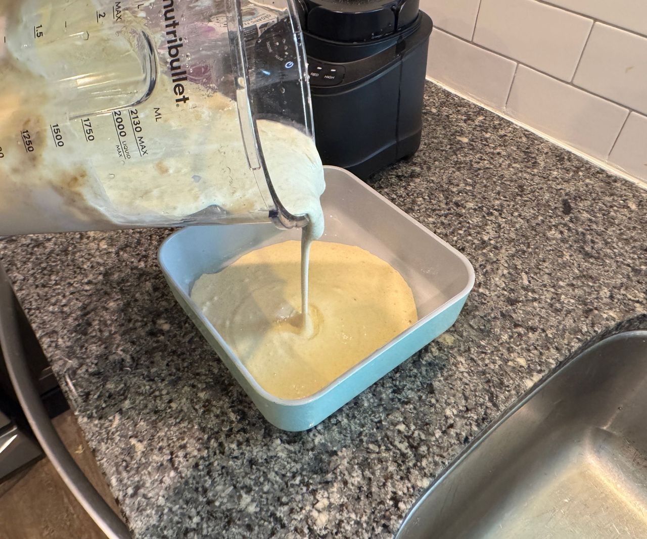 Pouring batter from a blender pitcher into a square cake tin.