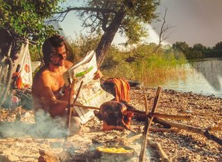 Julian Sayarer relaxes with a newspaper and food on the fire