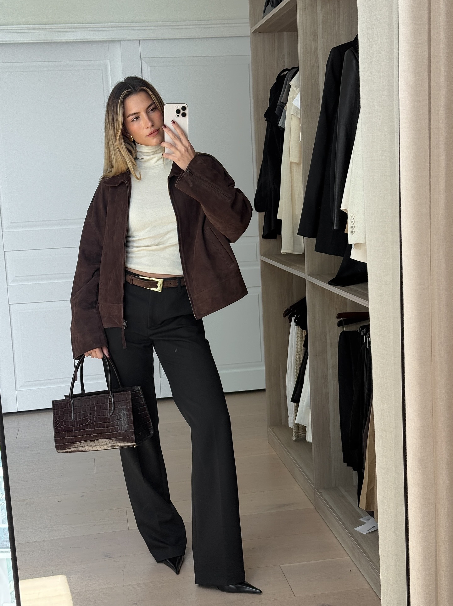 A woman taking a mirror selfie in an autumnal outfit with face-framing blonde highlights