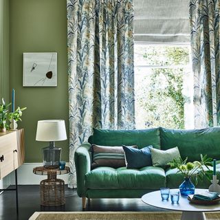 Green living room with sofa, patterned curtains and side table with lamp