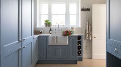 A utility room with blue built-in cabinets and a white farmhouse sink beneath a large framed window. 