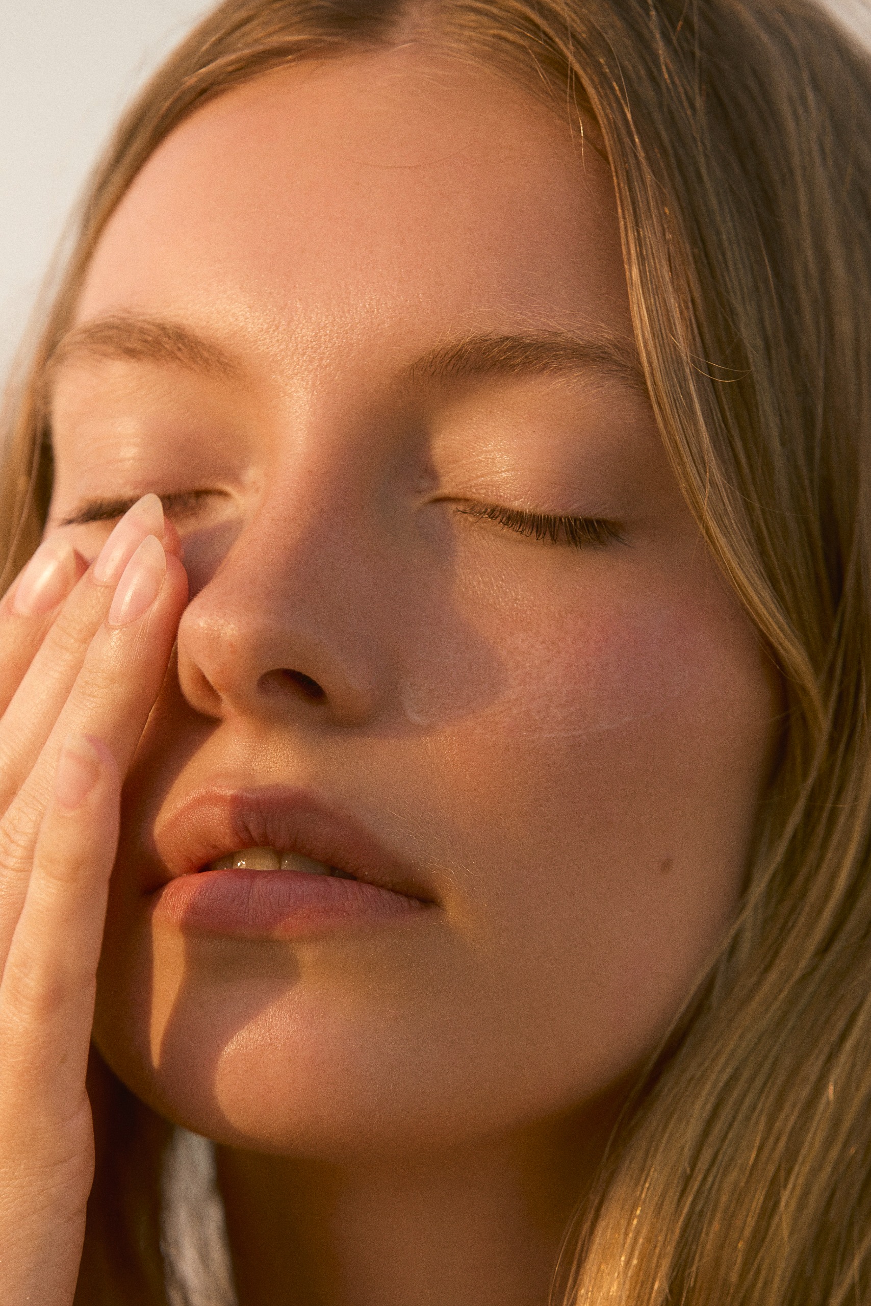 A woman touching her eye area with her eyes closed, wearing her natural nails