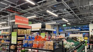 A photo of the black boxes that monitor customers in the Amazon Fresh shop hanging from the ceiling with shelves in the foreground and the exit in the background