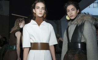 two female models one wearing a white dress and brown belt and the other wearing grey and black