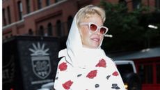 A headshot of pamela anderson wearing a white headscarf and sunglasses