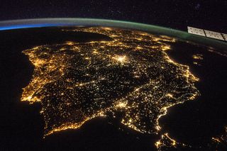 A photo taken from the International Space Station shows Portugal and Spain by night as a green aurora glows overhead.