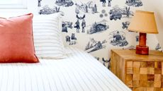 Bright bedroom featuring winter toile patterned wallpaper, a natural wood bedside table, and a bed styled with pinstripe bed linens