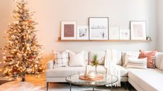 A minimalistic Christmas living room with a white couch, wall art, coffee table, and lit Christmas tree