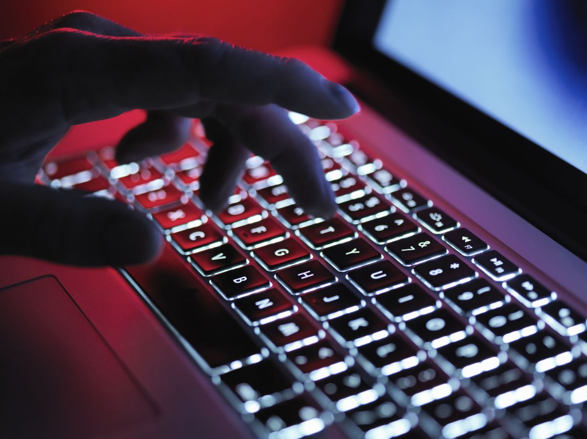 Hacker&#039;s hand hovering over an illuminated MacBook keyboard - an image denoting hacking