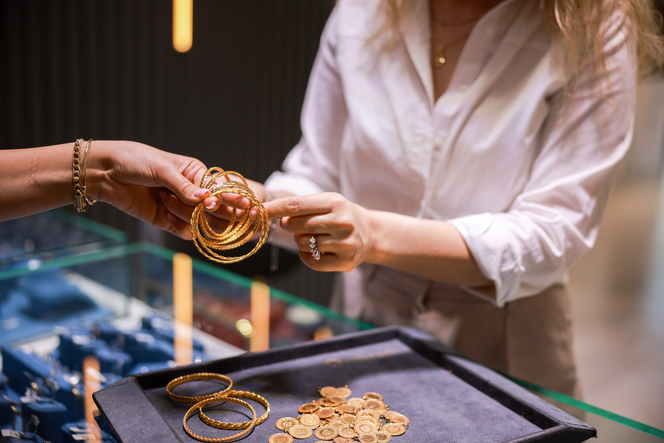 A female clerk in a high-end jewelry store is trying on a gold bracelet to show to a customer.