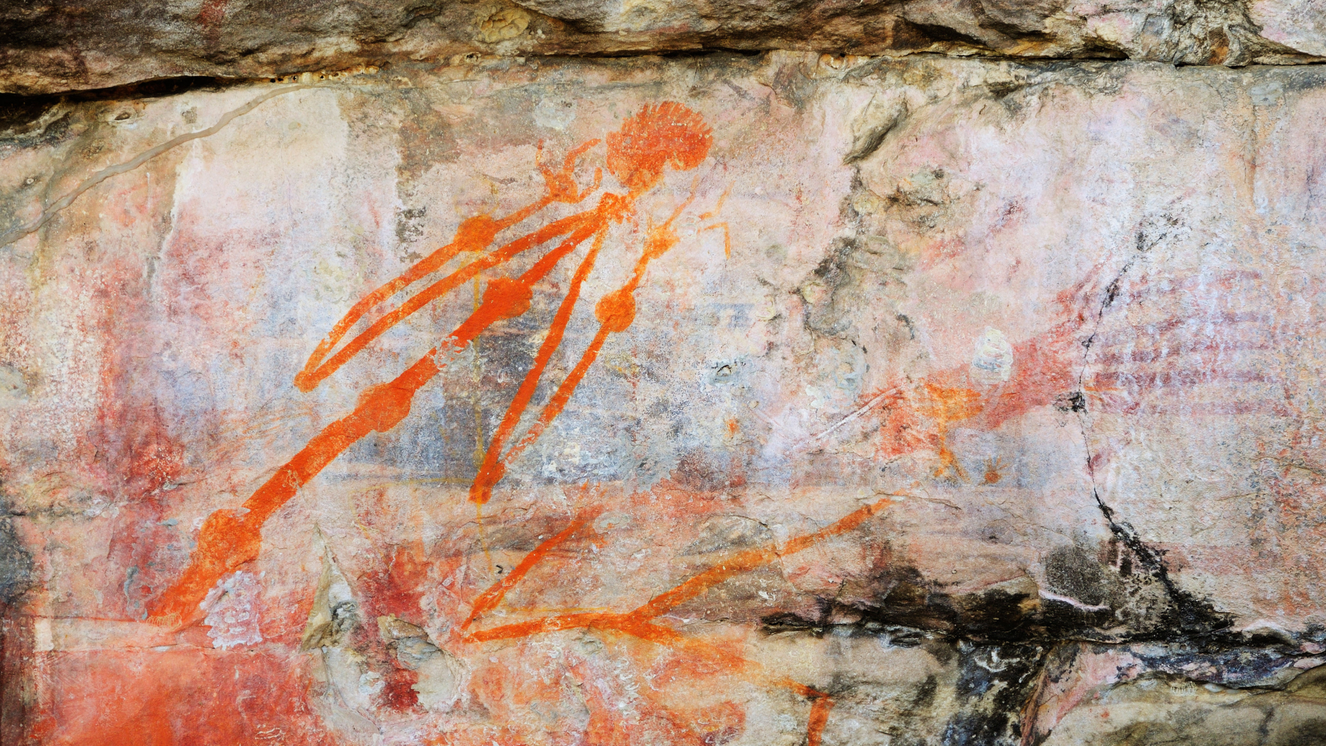 A light-colored wall of rock marked with bright orange drawings of a stick person and a hand