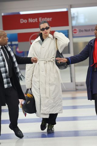 A photo of Dua Lipa wearing an off-white insulated trench coat with Puma sneakers, black sweatpants, a Chanel hobo bag, and a black Birkin.