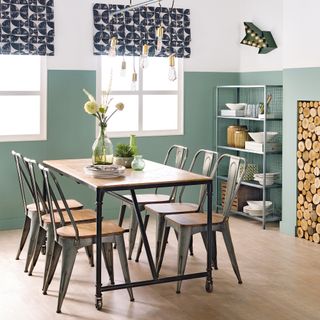 Green dining room with open shelving, log storage in fireplace and wooden dining table and chairs