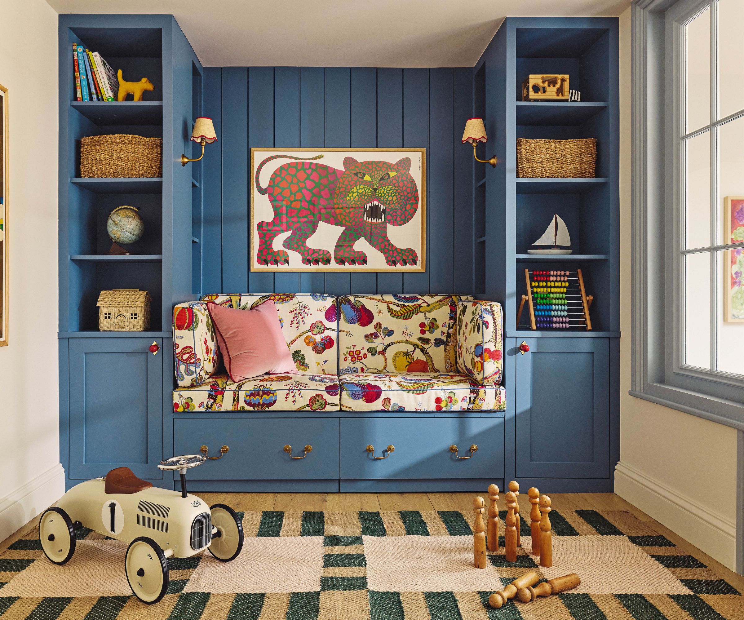 Kid's playroom with built in storage painted in blue with a bench upholstered in a patterned fabrics. There's a playful tiger print above the bench and a striped blue and jute rug on the floor