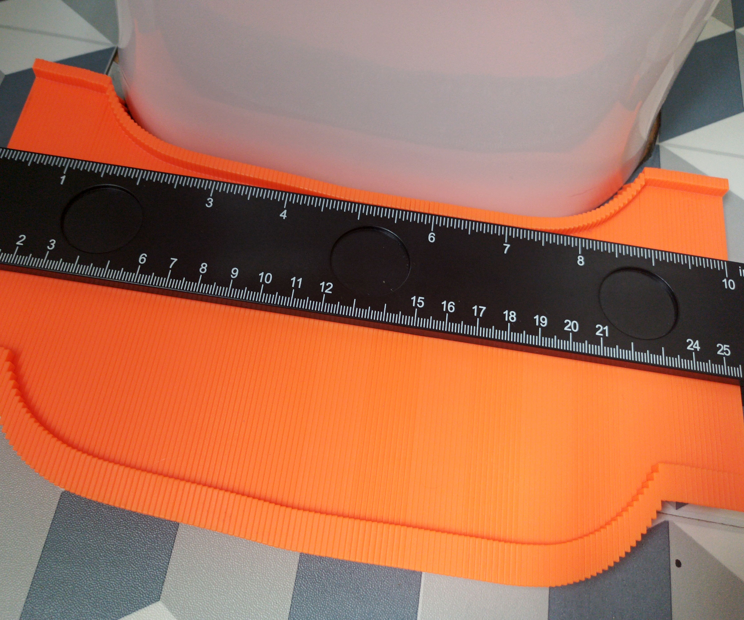 Orange and black contour gauge recreating curve of toilet base on gfloor