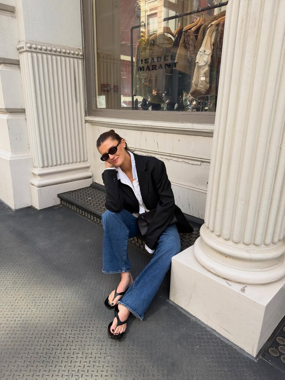 Woman in a blazer, jeans, and leather flip-flops.