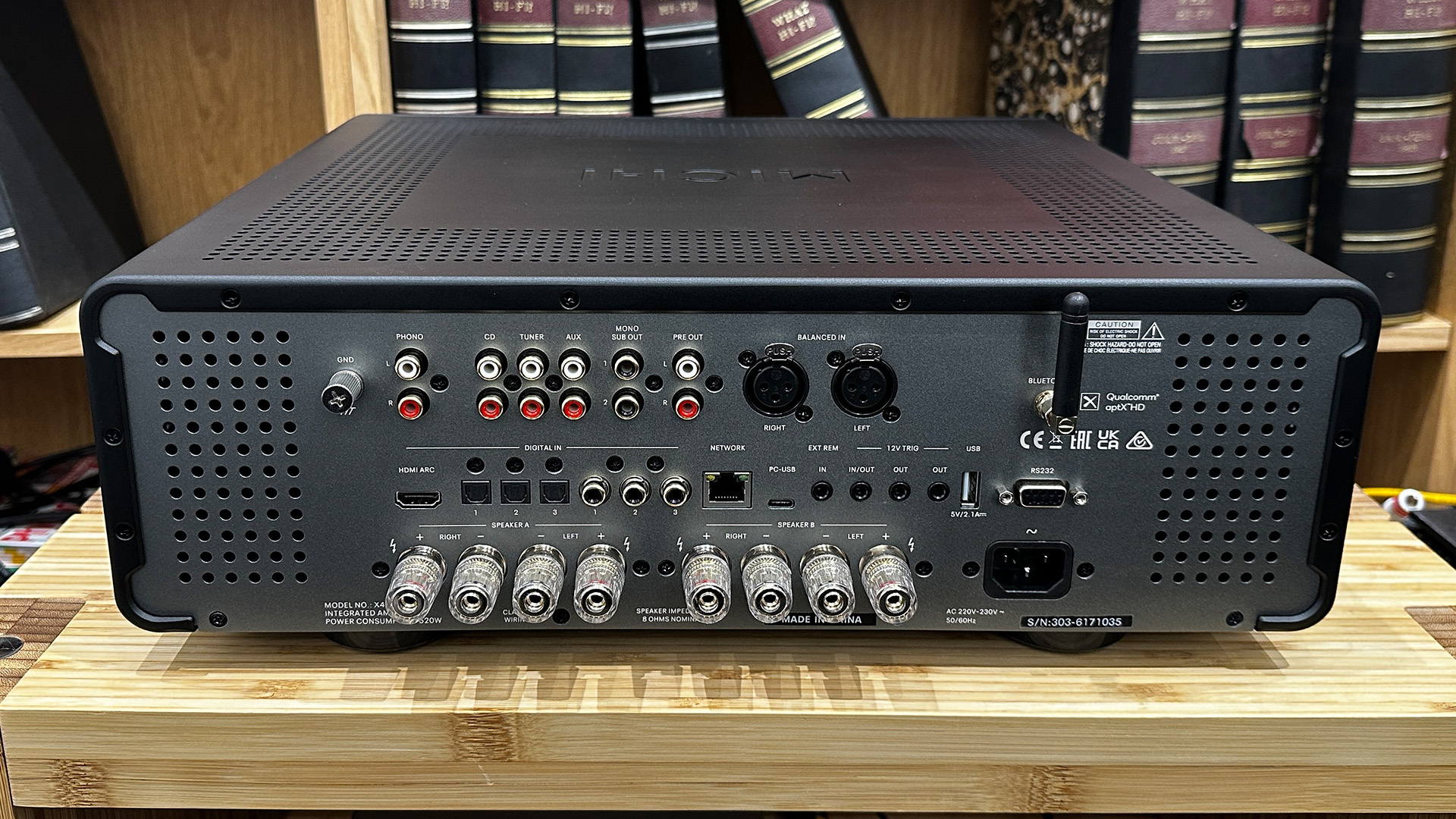Rotel Michi Prestige X430 integrated amplifier on wooden hi-fi rack in front of bookcase, rear of unit showing connections