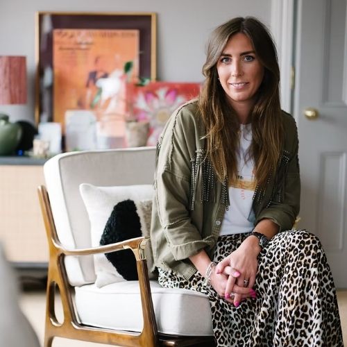 Girl in a cheetah print skirt and khaki jacket sitting in a white chair.