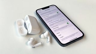 AirPods Pro 2 on a table next to an iPhone showing the volume control settings screen