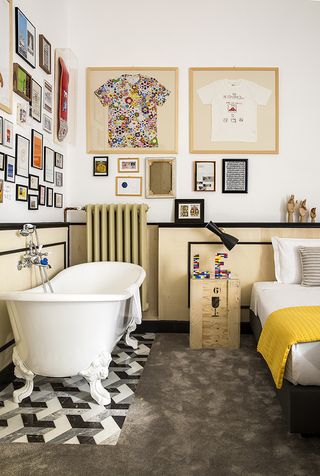 Bedroom featuring two framed t-shirts, a free-standing bath on geometric flooring, and bed with yellow throw