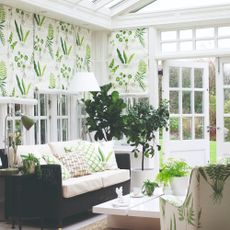 A white conservatory with botanical-print roller blinds covering the windows and matching with the armchair