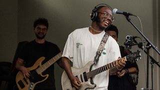 Justus West wearing headphones and playing guitar with a bassist