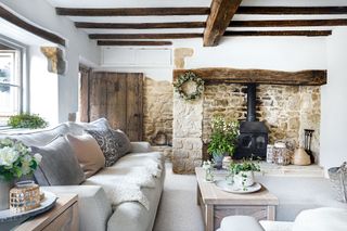 living room with pale sofas and beams and exposed stone walls with inglenook fireplace and old front door open
