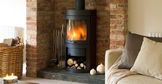 Beige living room with a brick fireplace with a log burner lit next to a beige sofa