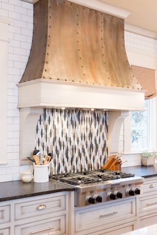 White kitchen cabinets with stove top and backsplash in three colors, hood, and white tiled wall