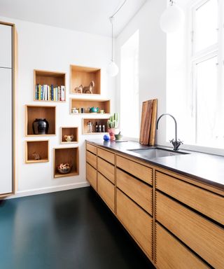 A modern kitchen with natural wood cabinetry and dark green linoleum flooring