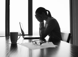 A black-and-white photo of a woman sitting in a office looking stressed and sad.