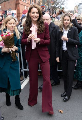 Princess Kate an an appearance in Boston wearing a wine red suit with matching pumps and a pink bow blouse