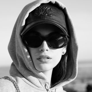 Kaia Gerber wears a leather celine baseball cap and a hooded sweatshirt in front of a Malibu beach