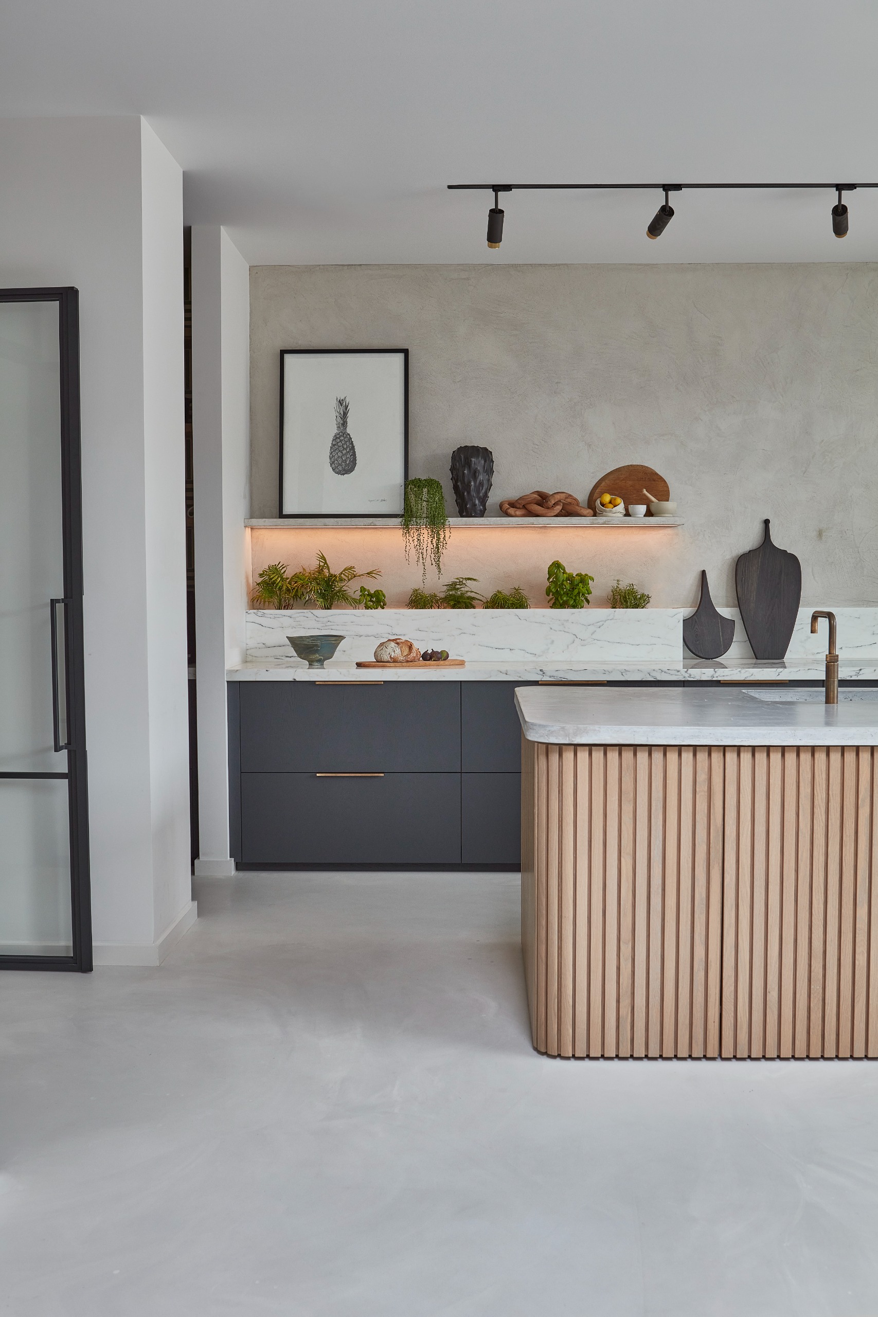 A clean spacious kitchen with a fluted wooden island, ope shelving with trailing plants and layered lighting