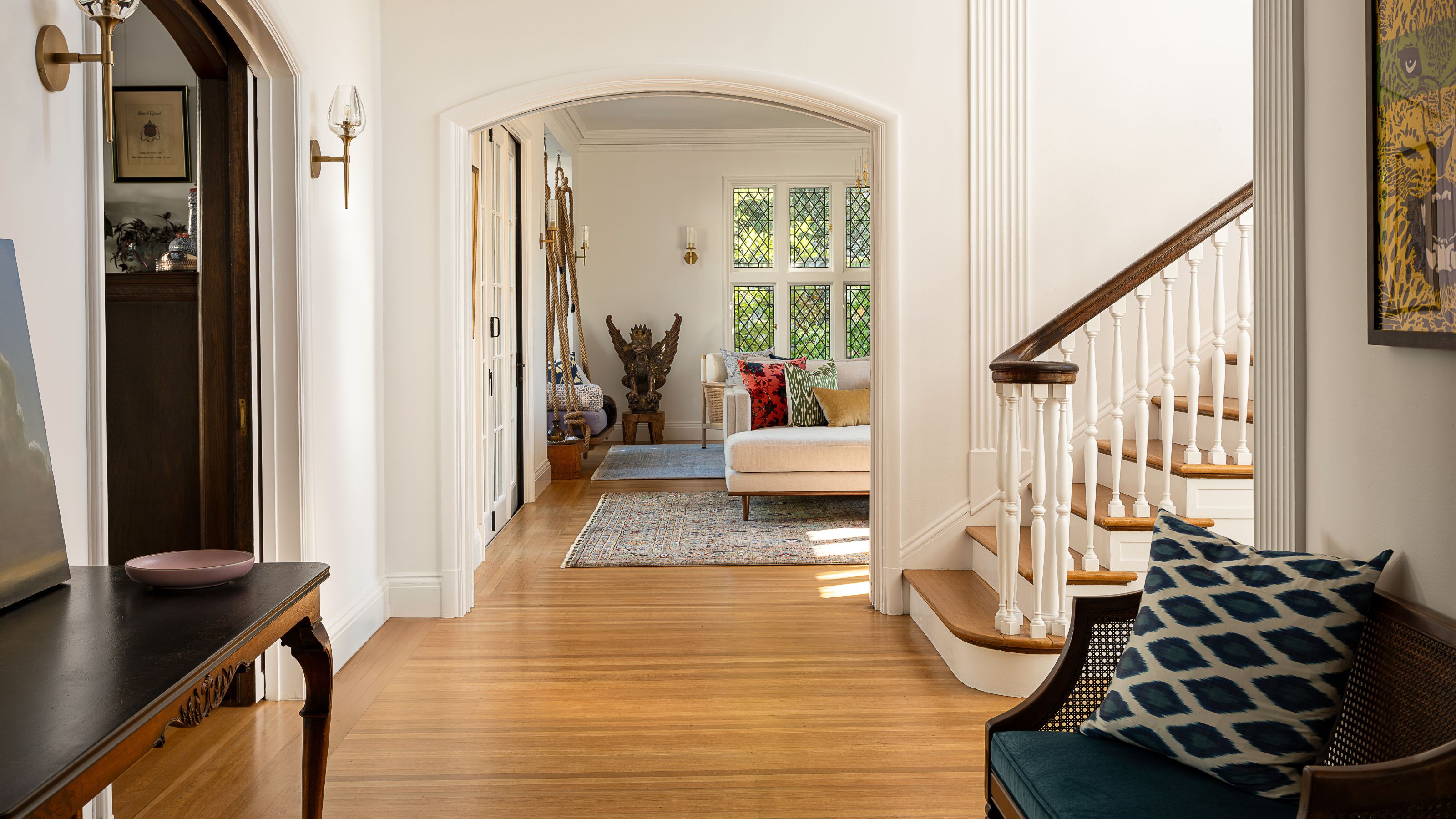 a neutral white painted entryway with arched doorways a sweeping wooden staircase and antique furniture
