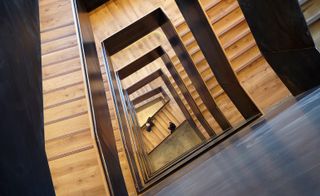 View looking down the center of a stair well going down numerous floor, stairs with wooden effect