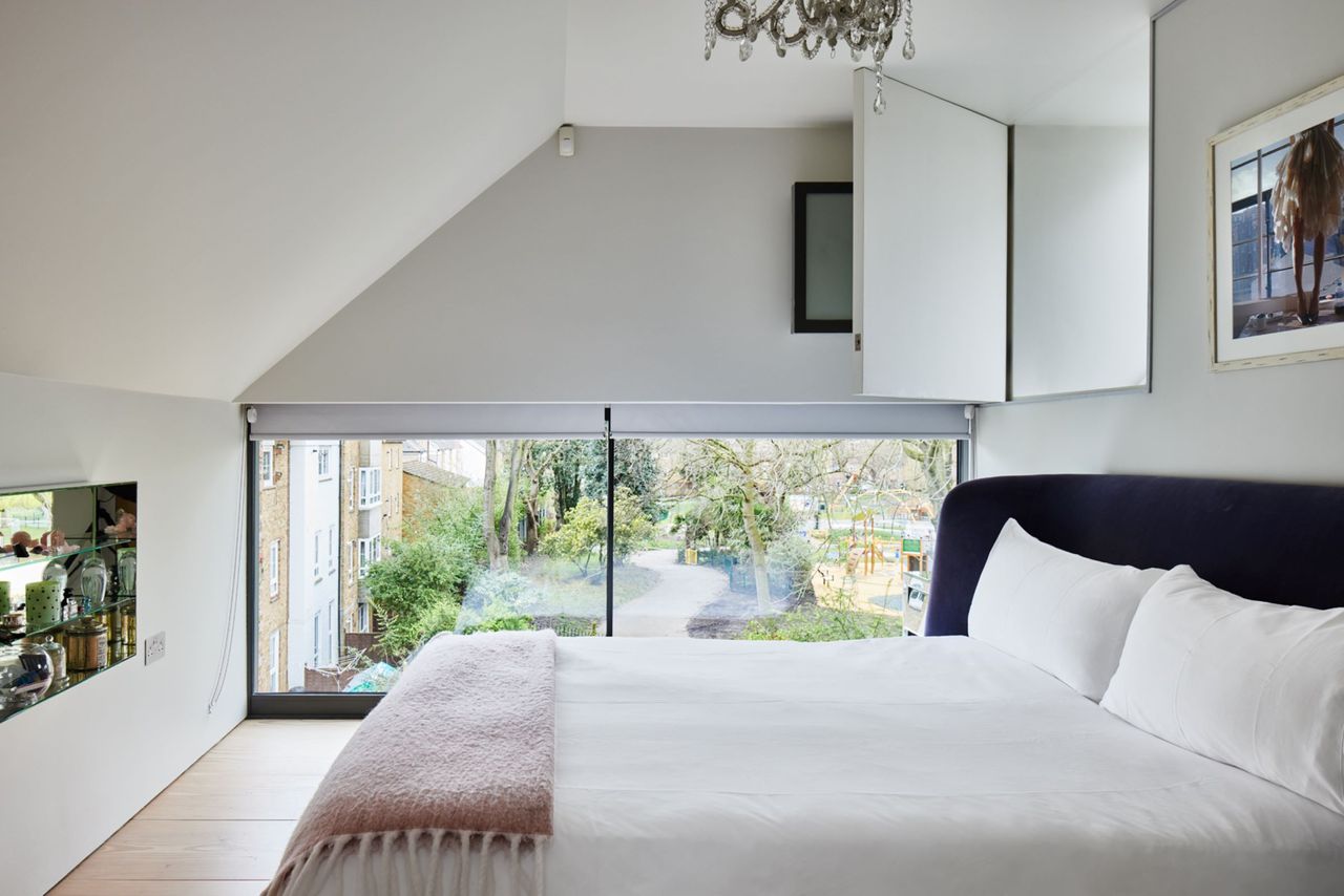 A white linen bed and glazed wall looking out onto a garden