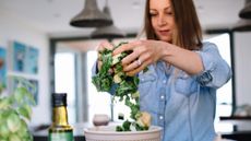 Woman in a kitchen using her hands to toss salad together over a bowl