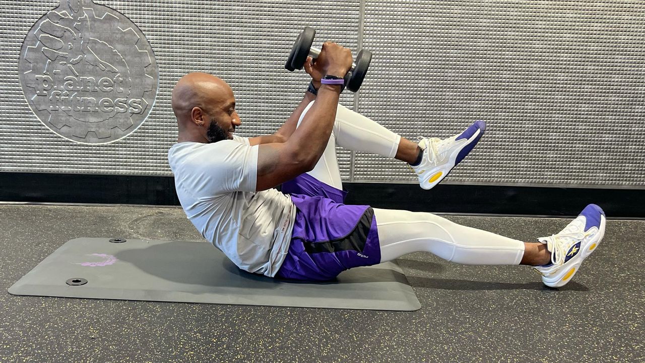 Teddy Savage performing a dumbbell floor chest fly to alternating knee tuck
