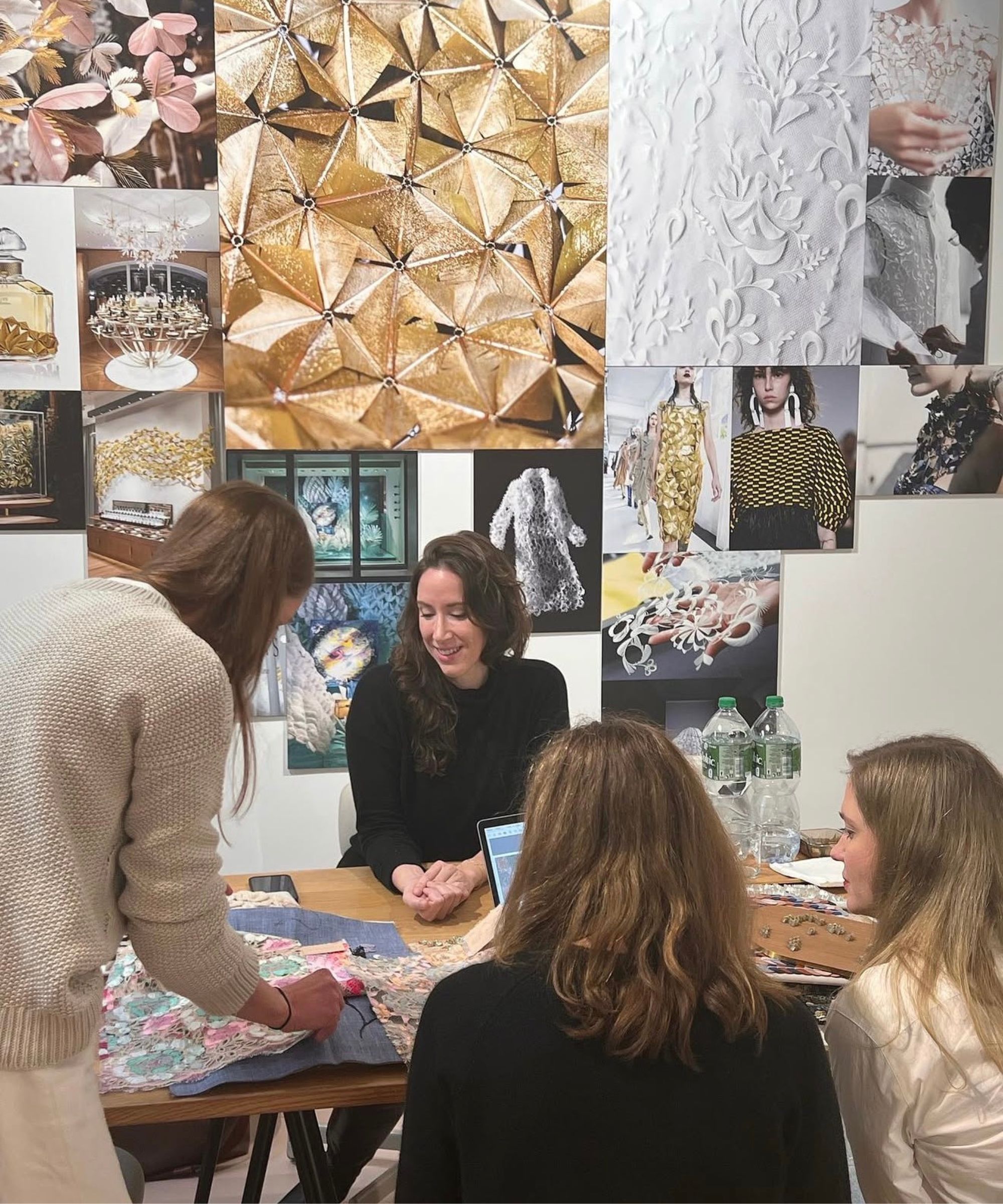 Group of women sat around a table looking over fabric samples, gallery wall in background of images