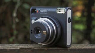 An Instax Square SQ40 camera, on a wooden surface in a woodland setting