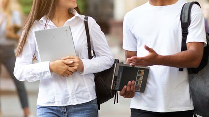 Student holding a Chromebook talking to a man