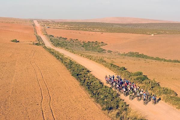 The peloton rolls across a gravel road.