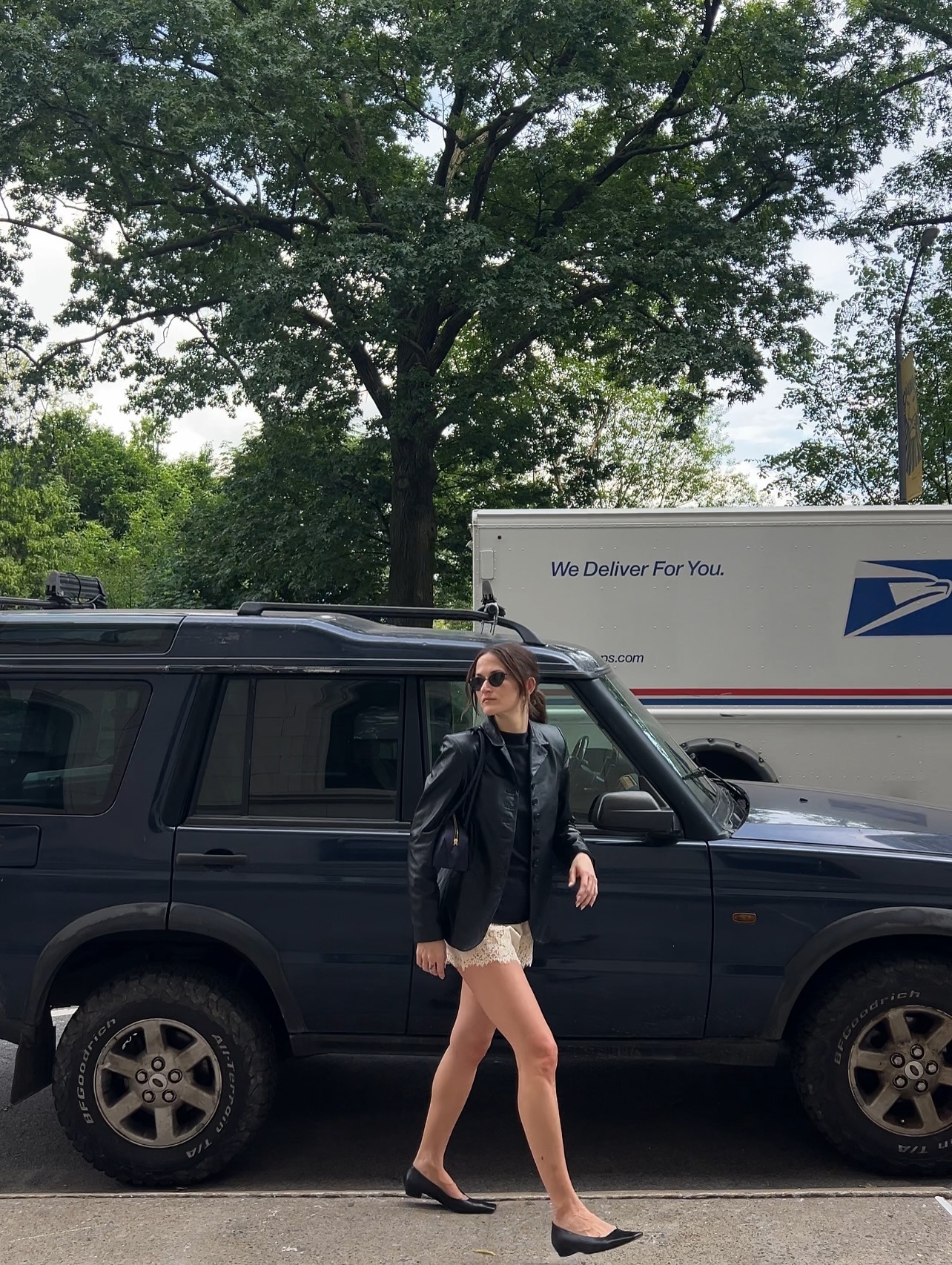 @elizagracehuber wearing a black leather blazer, navy sweater, and cream lace-trim shorts.