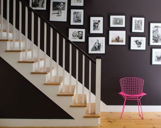 gallery wall of black and white family photos against dark painted wall and pink chair