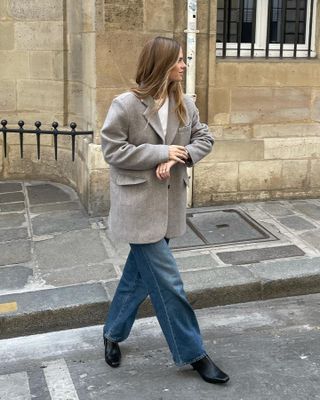 Scandinavian creative Clara Dyrhauge walks across the street wearing an oversize gray blazer, a white top, relaxed jeans, and black boots.