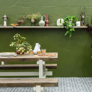 Green painted exterior wall with decorative vases display on a long open shelf and a wooden garden in front