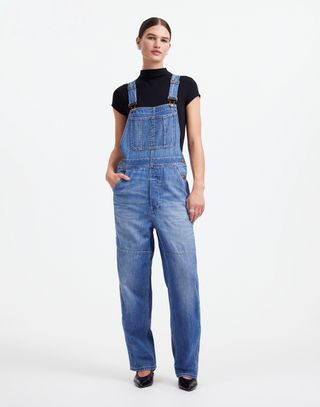 a model stands in front of a plain backdrop wearing madewell overalls designed by alexa chung