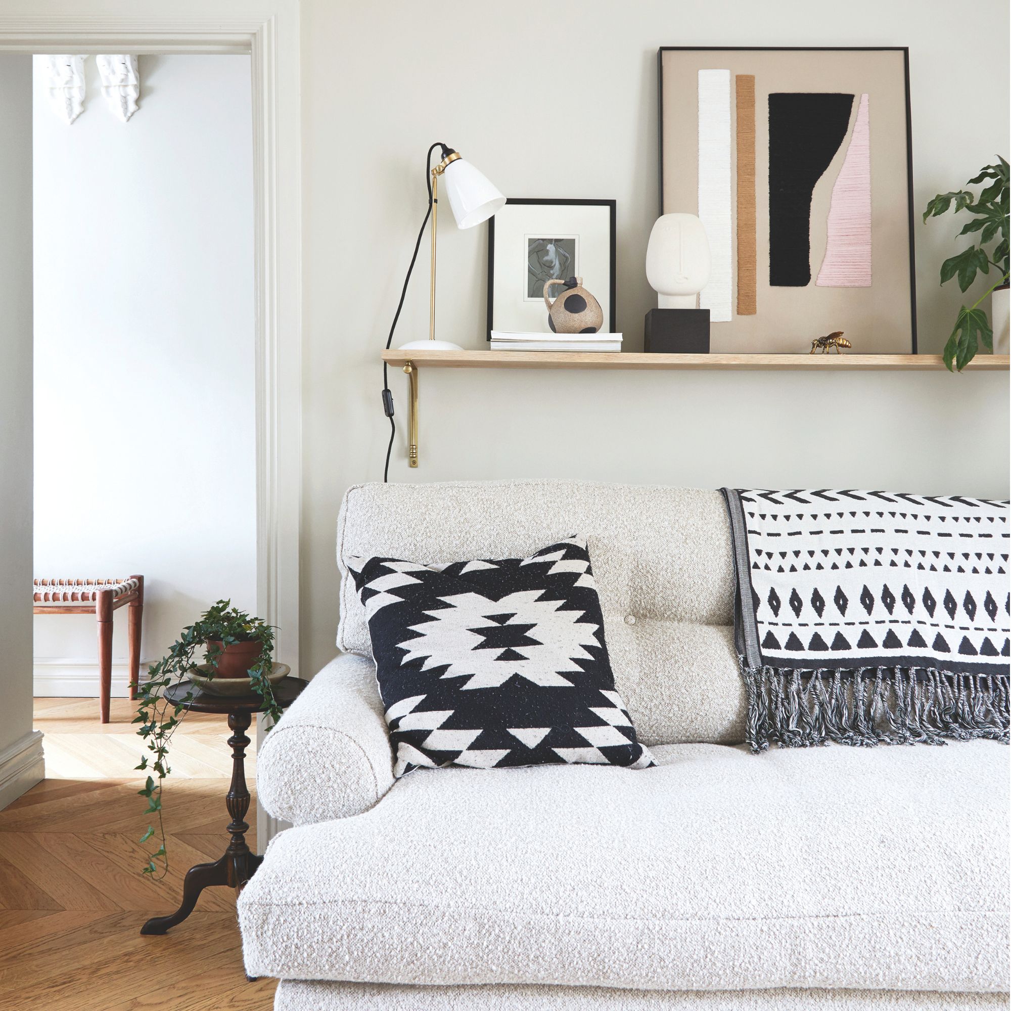 White painted living room with a white boucle sofa underneath a wooden wall shelf filled with home decor